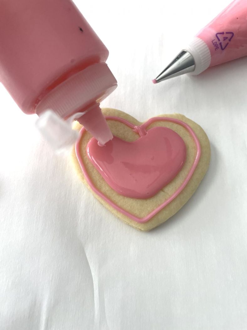 heart cookie with pink icing being squeezed into center